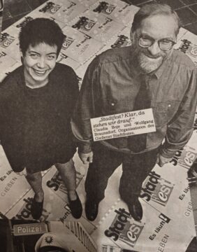 Schwarzweisbild aus einer Zeitung, eine Frau und ein Mann, von oben fotografiert. Beide lächeln in die Kamera.