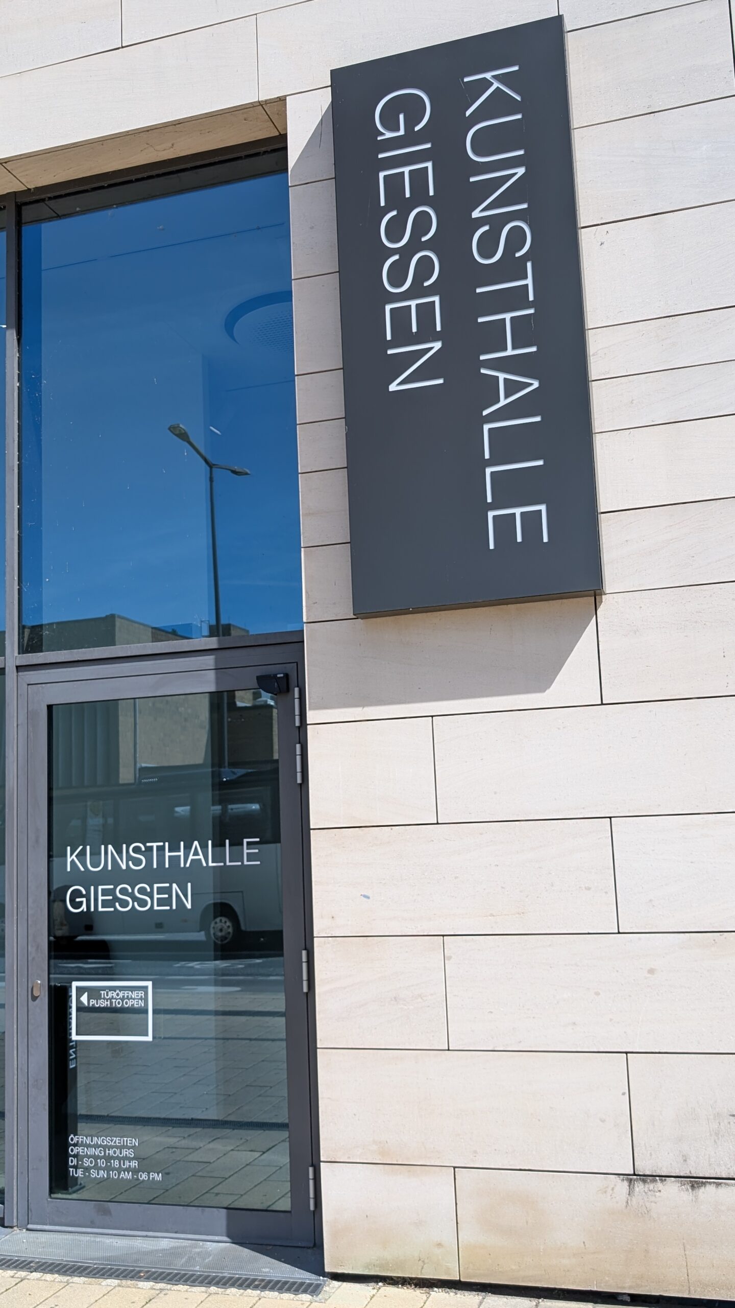 Eine Glastür, an der Wand daneben ein Schild mit der Aufschrift "Kunsthalle Gießen"